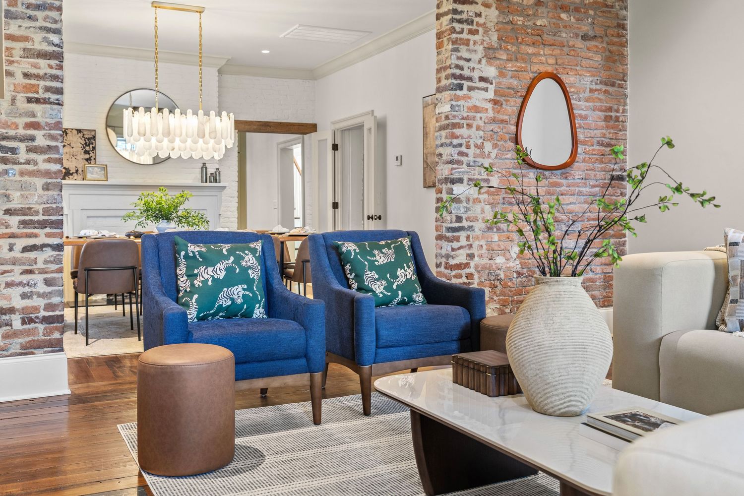 Modern living room with blue velvet chairs, exposed brick columns, hardwood floors, and elegant chandelier.