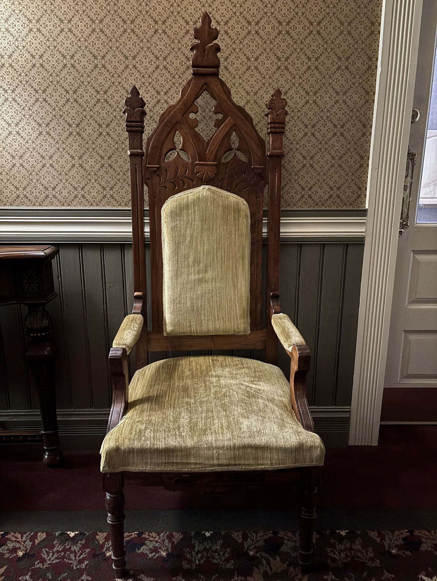 Antique Gothic Revival wooden armchair with ornate carved details and green velvet upholstery in a Victorian interior in the Beaumont hotel