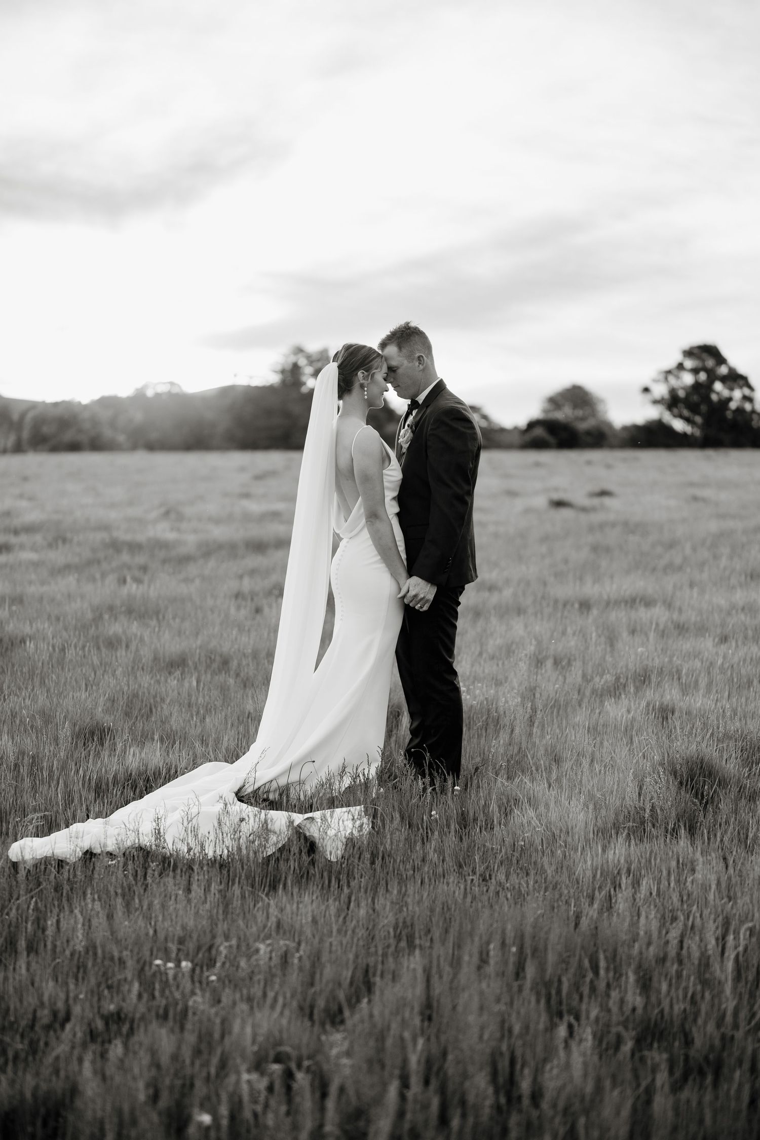 Black and white photo of a bride and groom standing in a field, sharing an intimate moment in wedding attire.