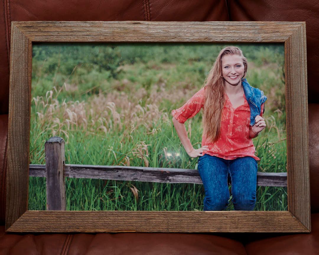 High school senior sitting on fence with grassy field background, printed on metal print with barnwood frame.
