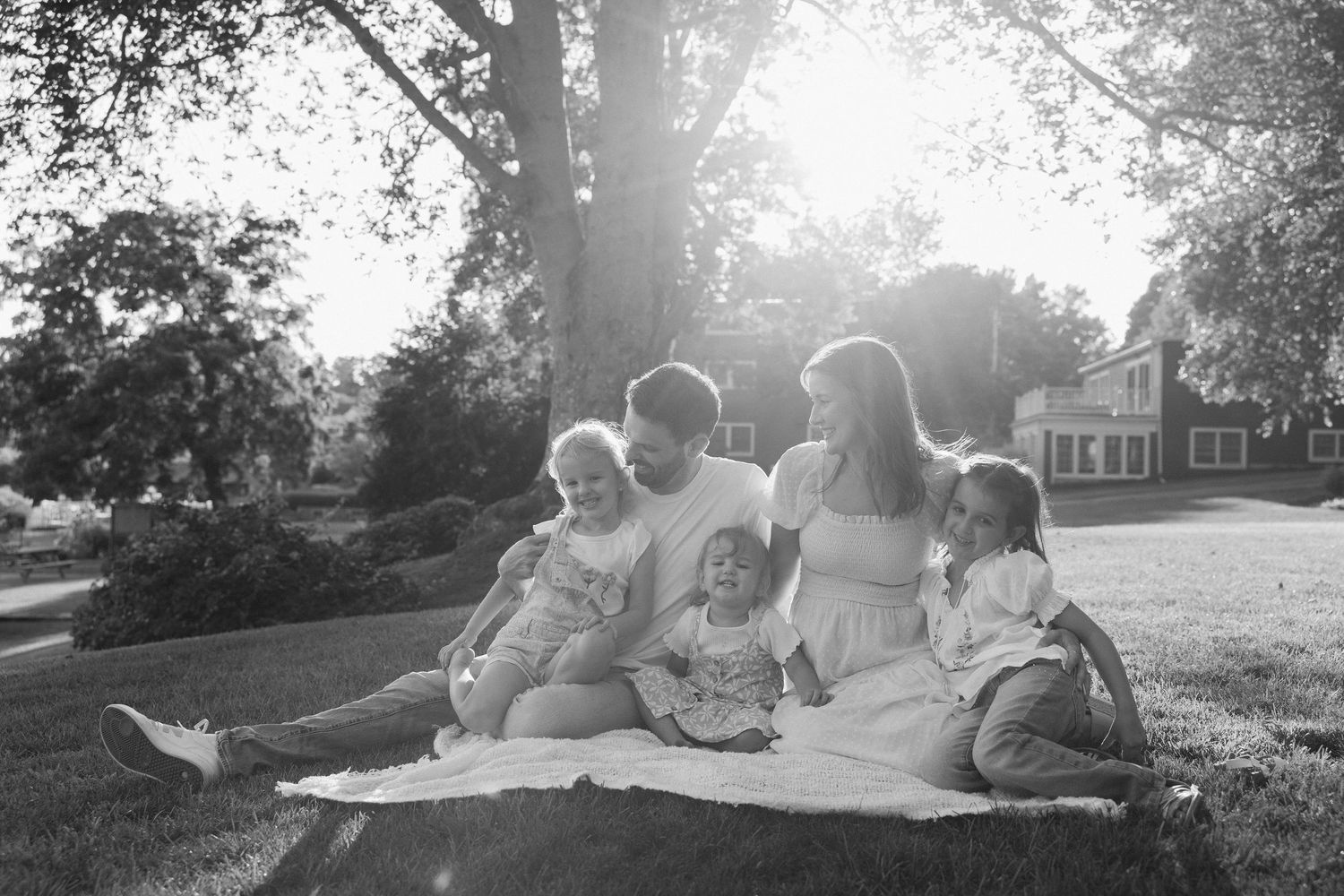 Black and white family photo of parents with three young children sitting on a blanket in a sunny park.