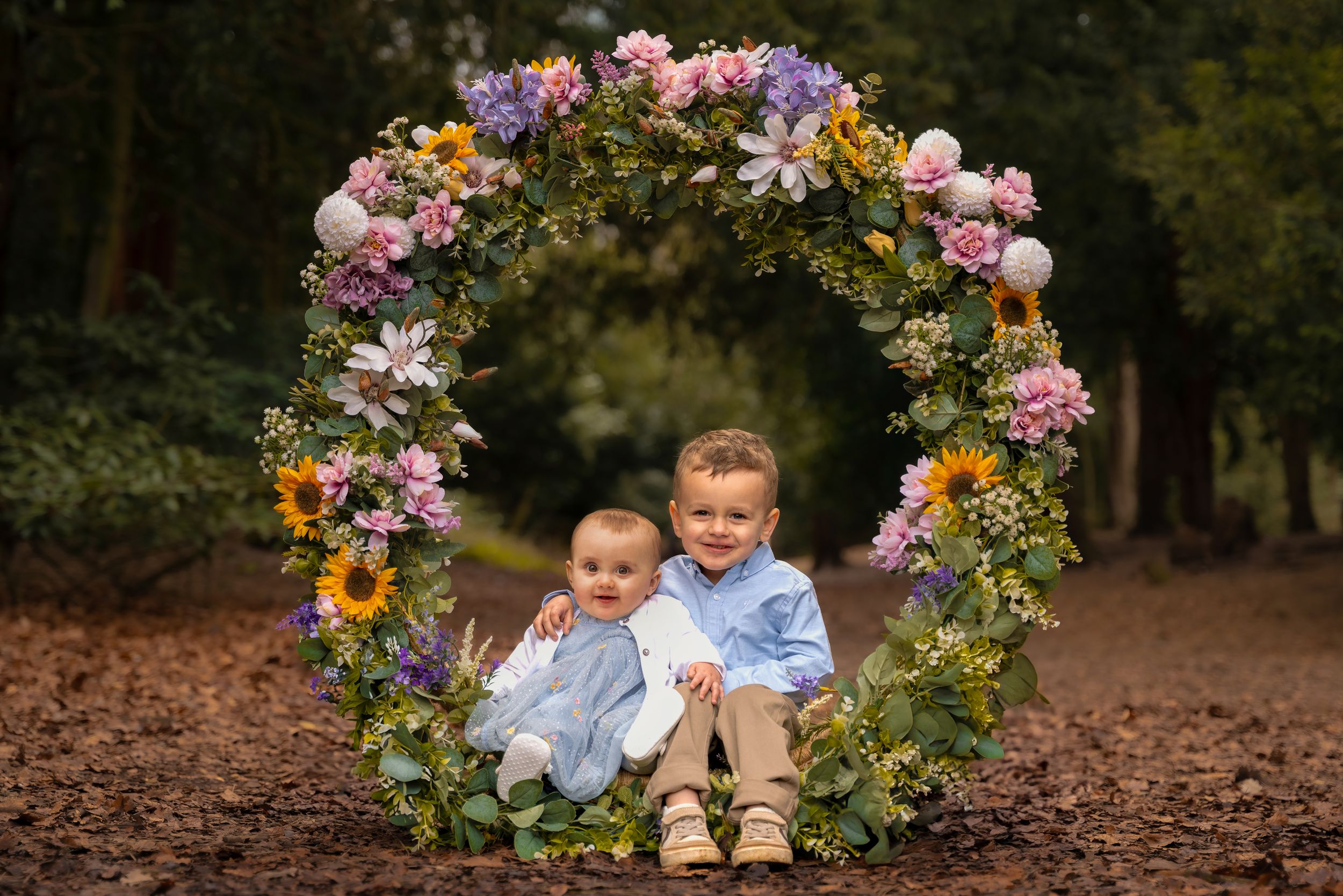 Two children sit inside a large floral wreath with colourful flowers during a childhood photography session in Lincolnshire.