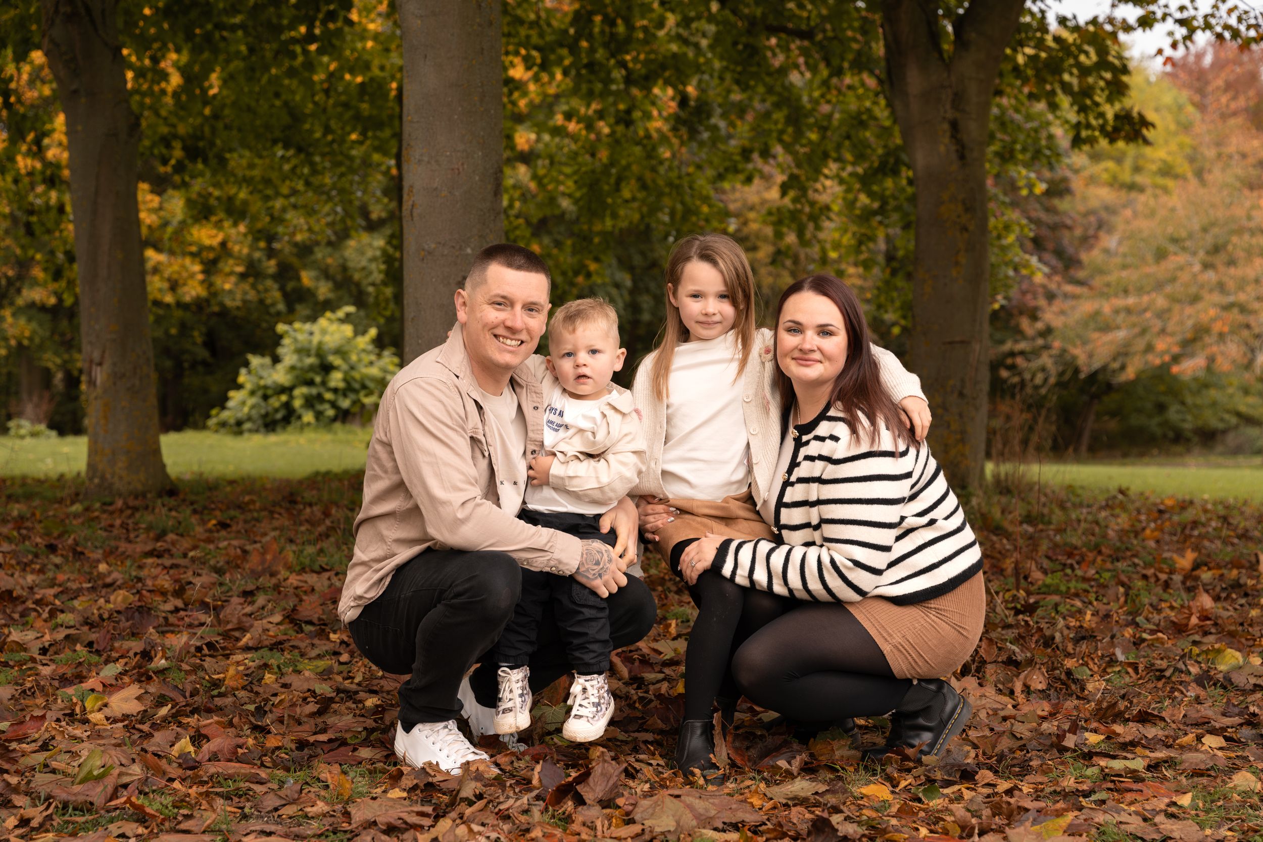 Family of four posing outdoors in autumn park with colourful fallen leaves during a family photoshoot in Lincolnshire.