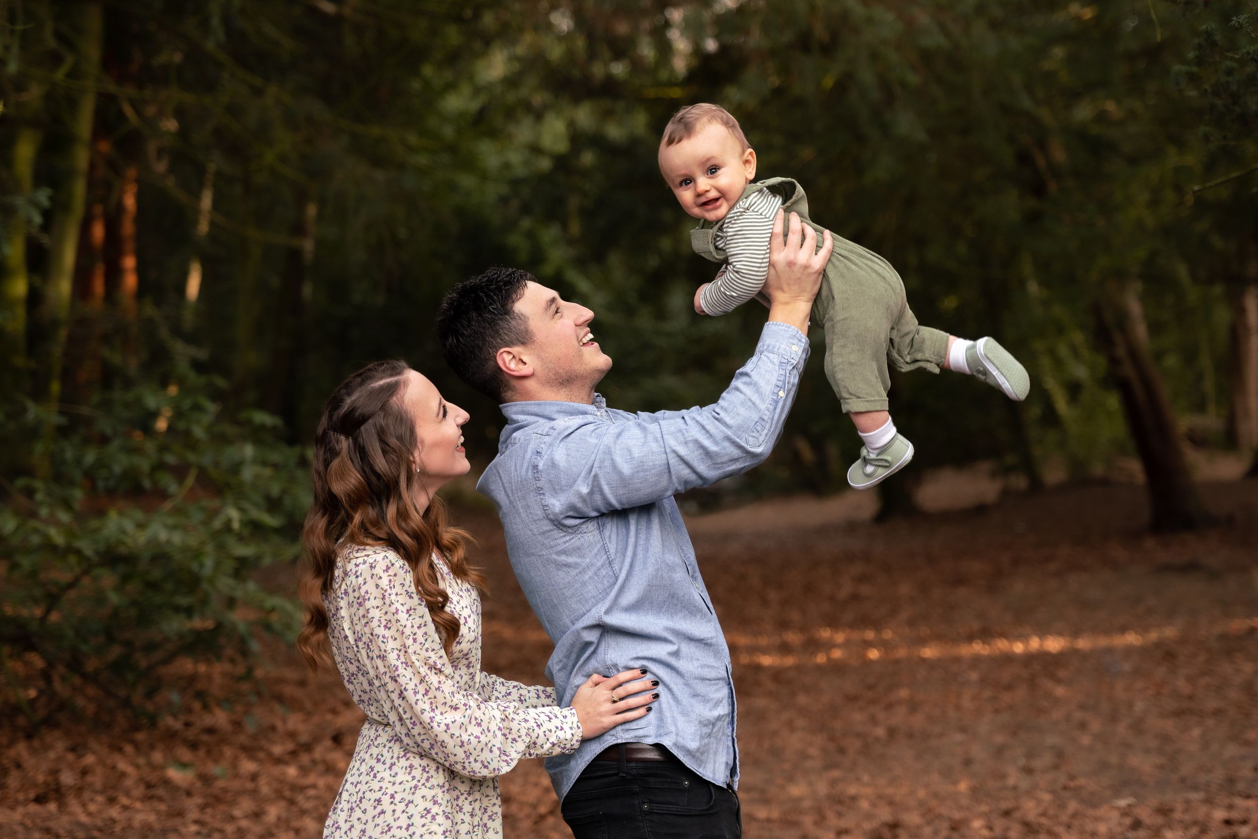 A joyful family outdoors, father lifting smiling baby in air while mother watches during a family photoshoot in Lincolnshire.