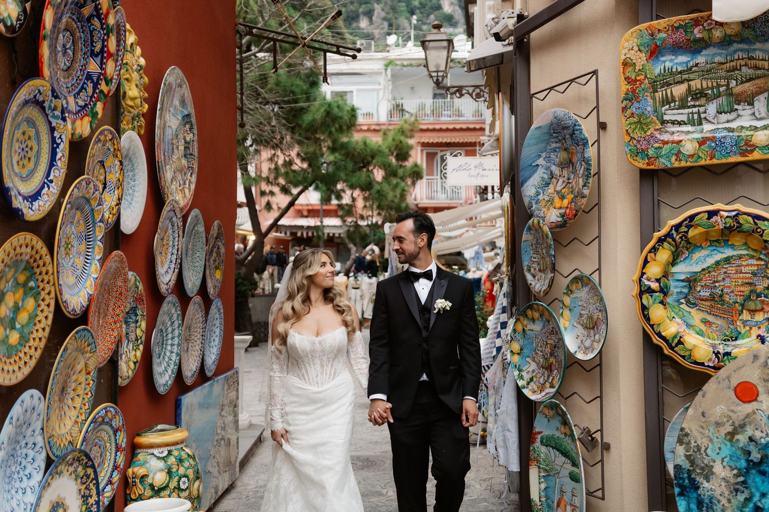 Bride and groom walk hand in hand through a colorful ceramic shop in Positano, Italy, on their wedding day.