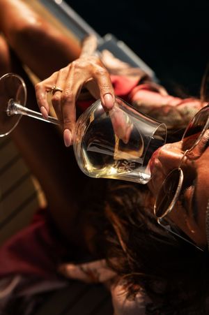 Hands pouring wine between glasses on wooden boat deck in dramatic lighting.
