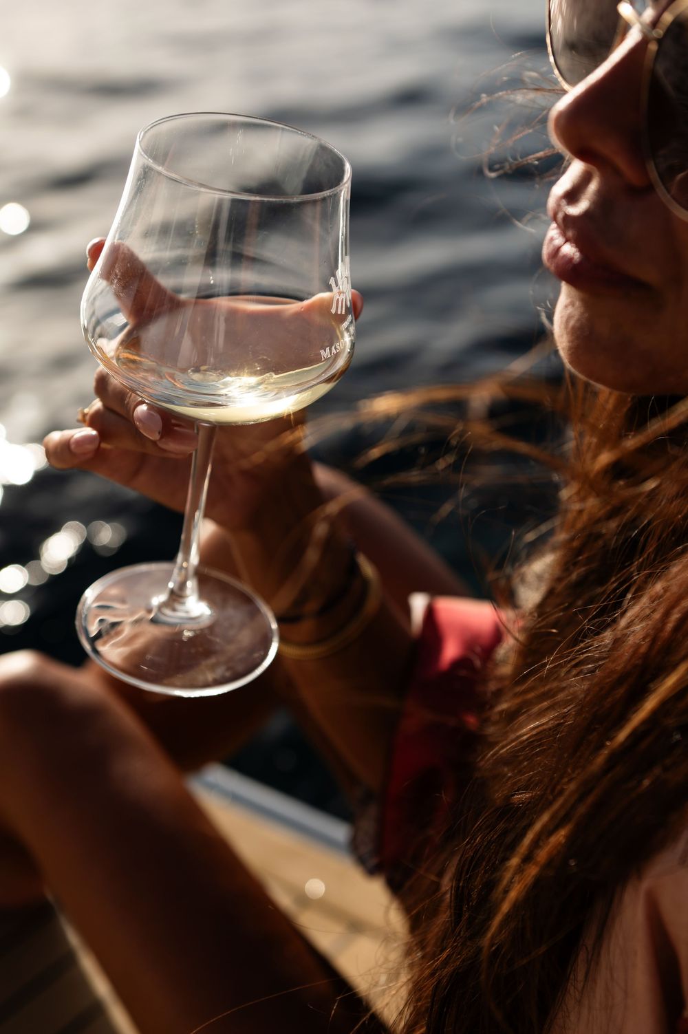 Person sips wine from a glass while enjoying a sunset on the water, creating a serene and relaxing moment.