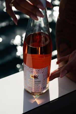 Bottle of rose wine with decorative label catching sunlight on boat deck.