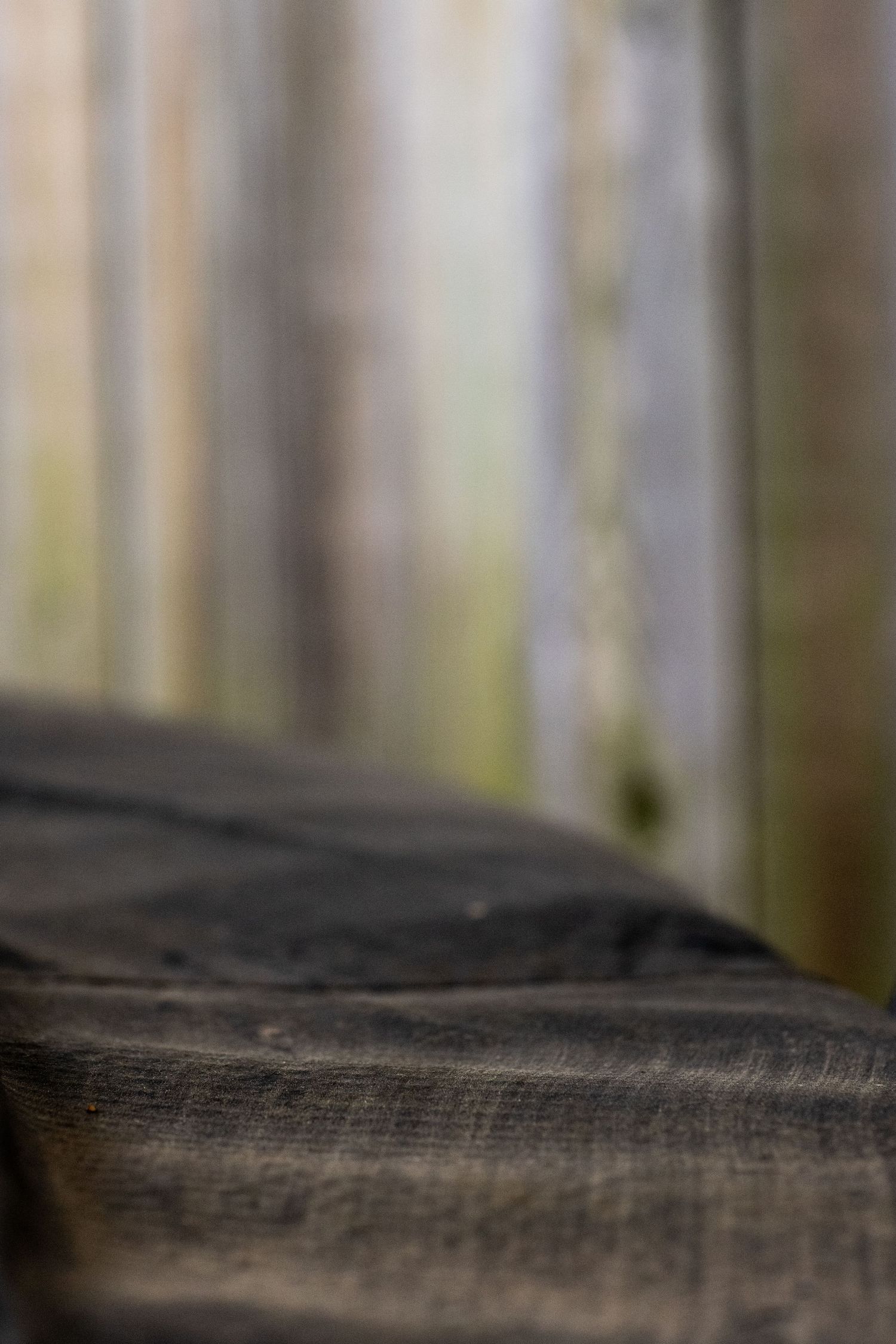 Close-up of dark textured burlap fabric with blurred wooden fence posts in soft bokeh background.