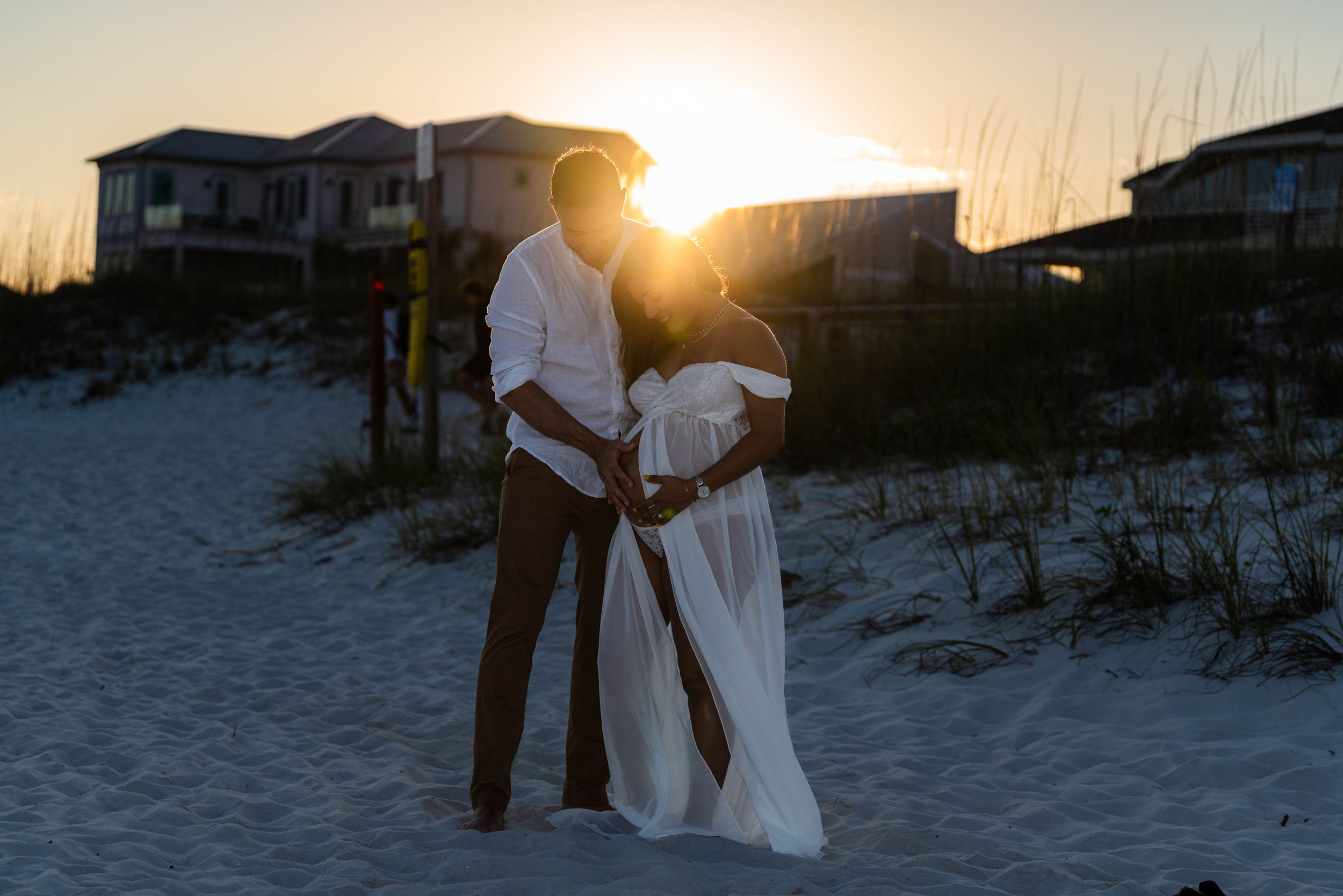 Pregnant couple embracing at golden sunset on white sand beach, maternity photo shoot.