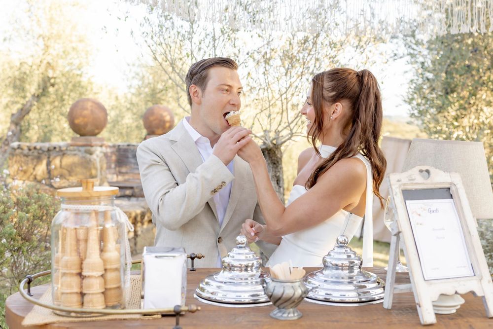 Bride feeding groom a cookie at an elegant outdoor dessert table during their wedding reception.