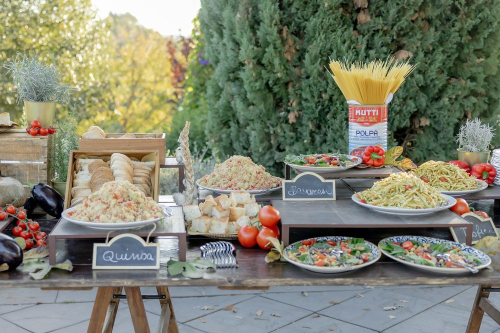 Outdoor Italian food buffet with pasta, salads, and fresh vegetables on wooden tables.