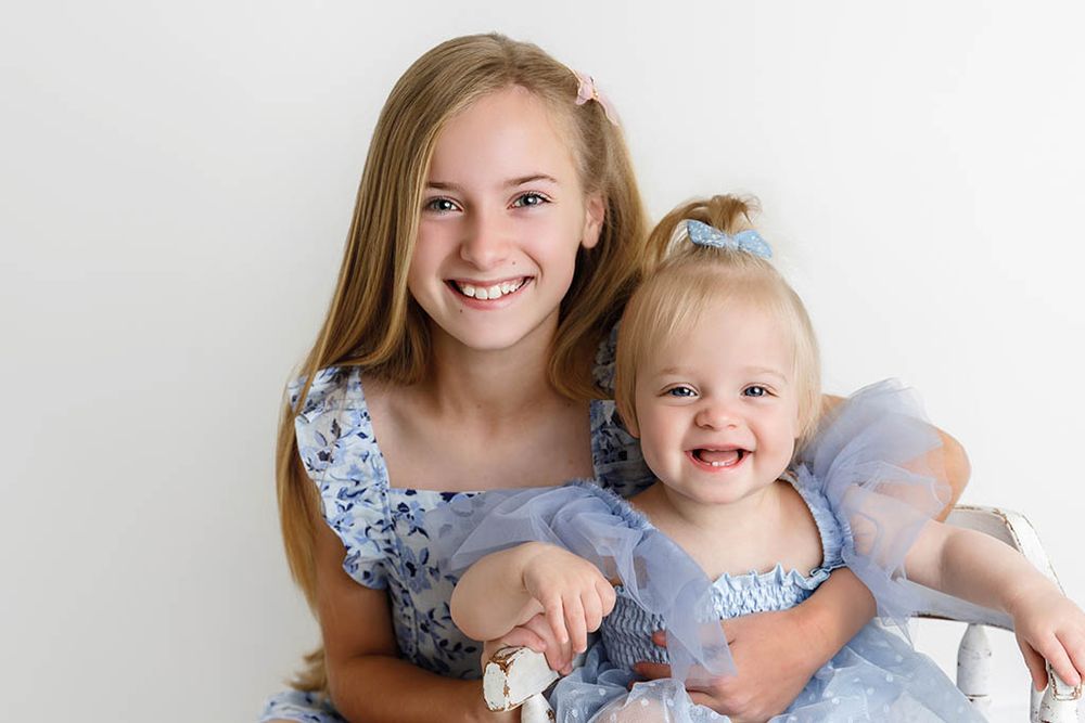 Sisters smiling together, wearing matching blue dresses for a portrait in Canyon Lake, California.