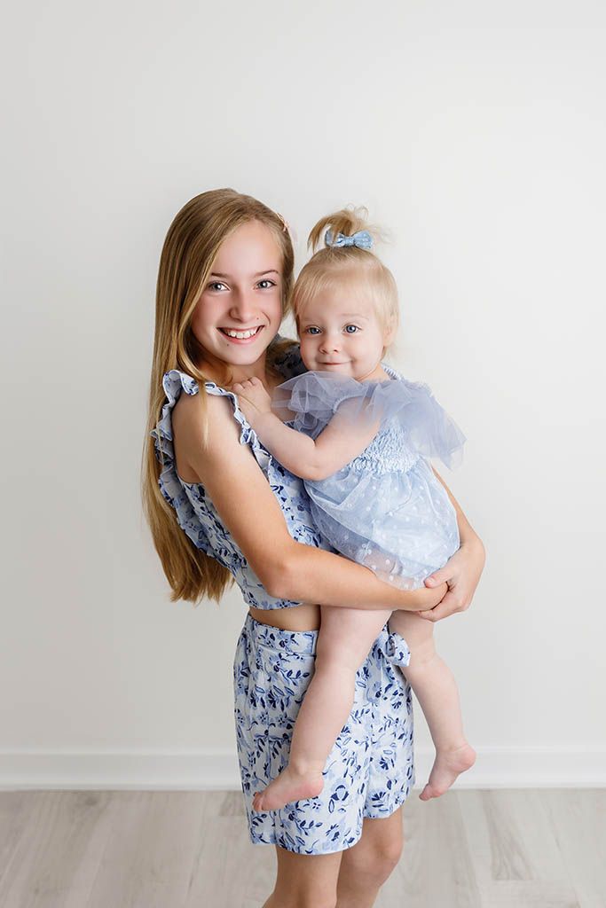 Big sister and baby sister smiling in professional portrait photography studio in Canyon Lake, California.