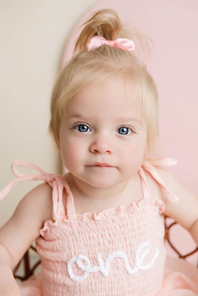 Adorable baby girl in pink smocked dress with bow headband celebrating her first birthday by Canyon Lake baby photographer.