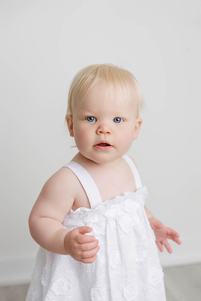 Canyon Lake baby Photographer photo of blonde baby girl with blue eyes wearing a white embroidered sundress.