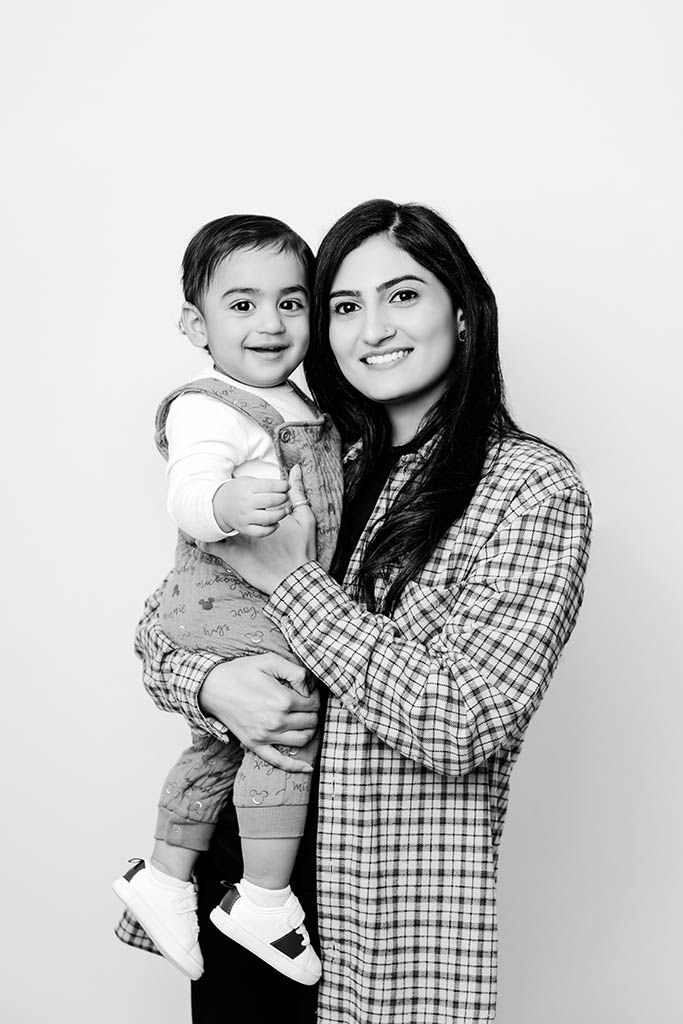 Black and white portrait of a smiling mom holding a happy toddler against a light background.