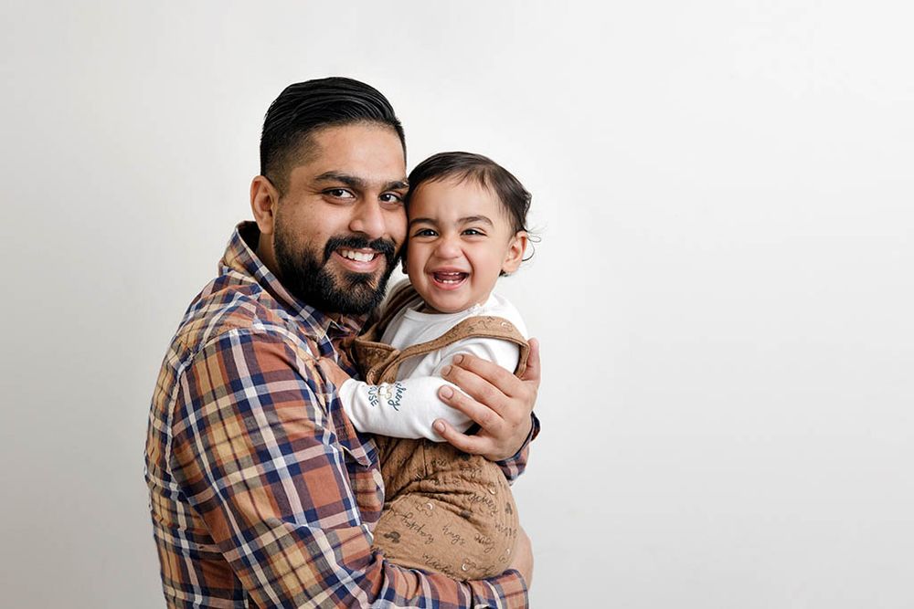 Smiling dad hugging laughing toddler against white background.