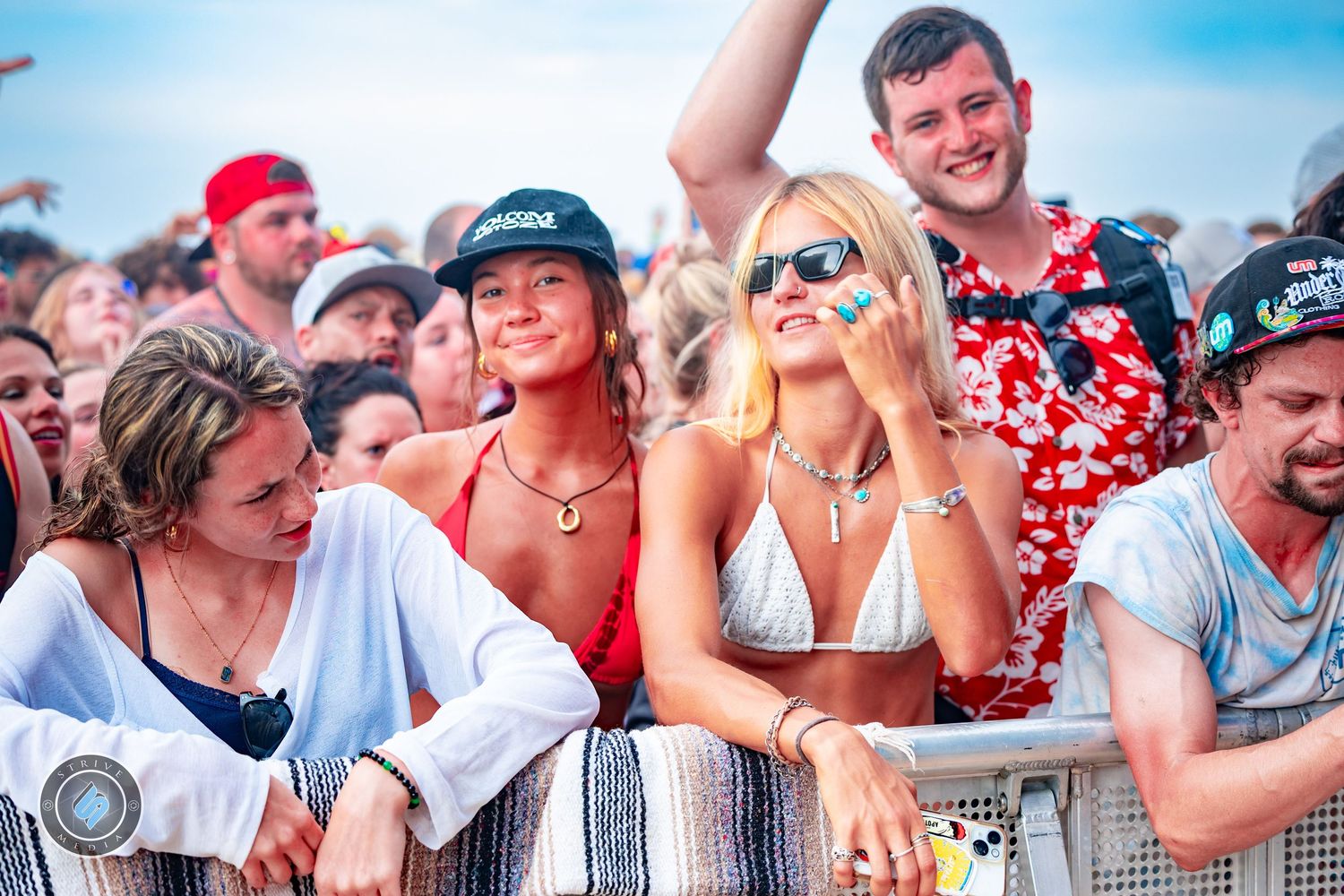 Excited festival crowd leaning on barrier fence enjoying outdoor beach music event.