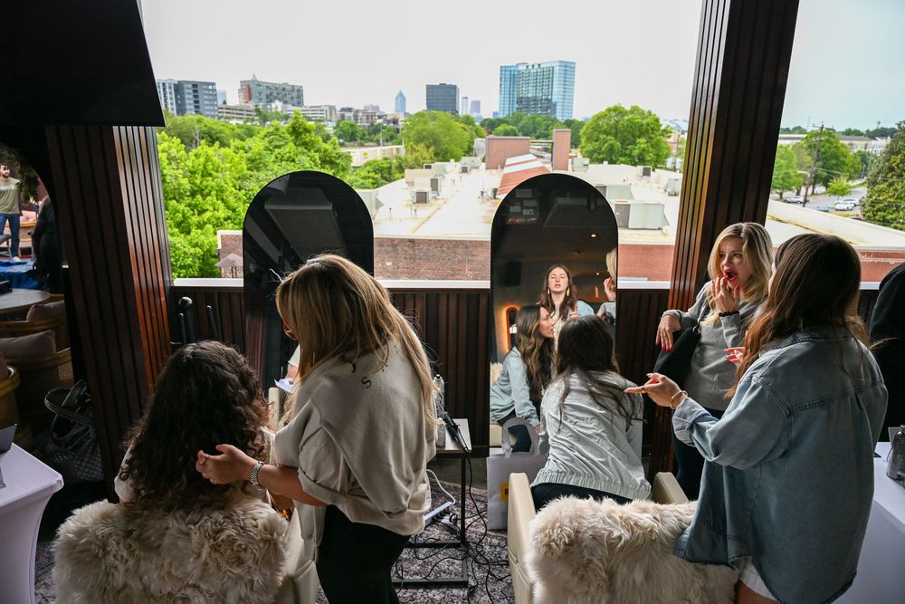 Hair stylists working with clients in a modern salon with panoramic city views and lush green trees outside.