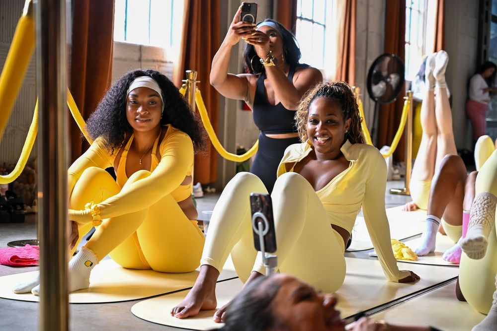 Women in bright yellow activewear smiling and posing on gold mats during a fun group workout session.