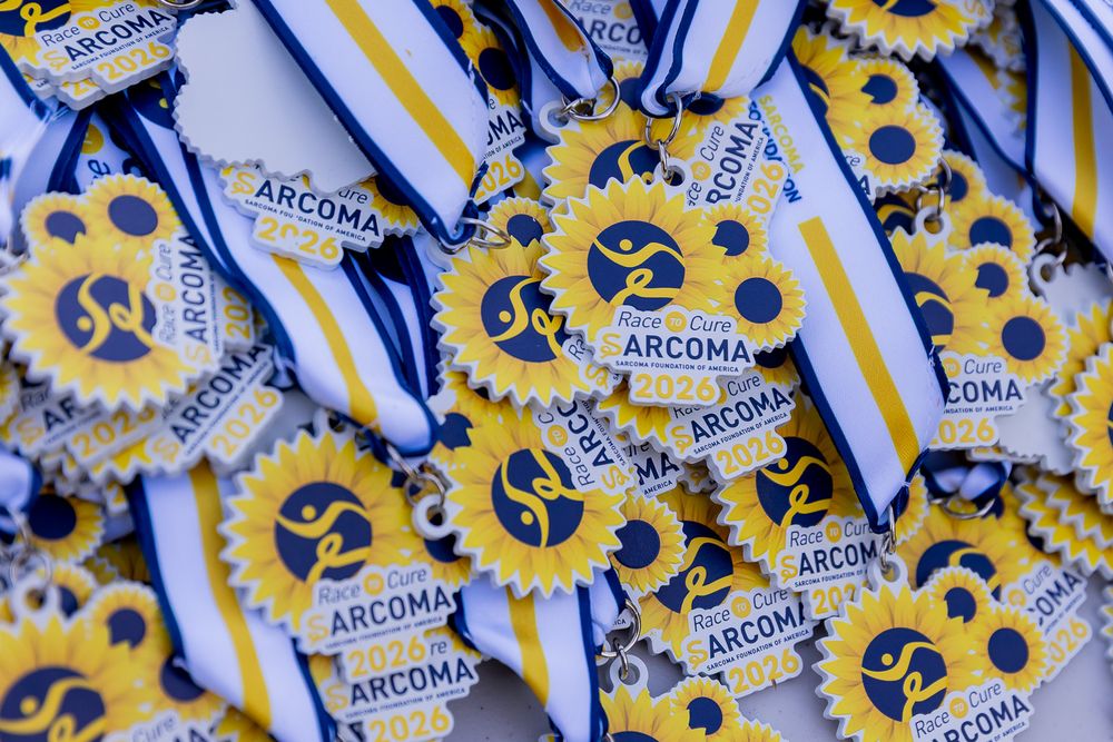 A pile of gold and blue ARCOMA medals with ribbons awarded at a sporting event.