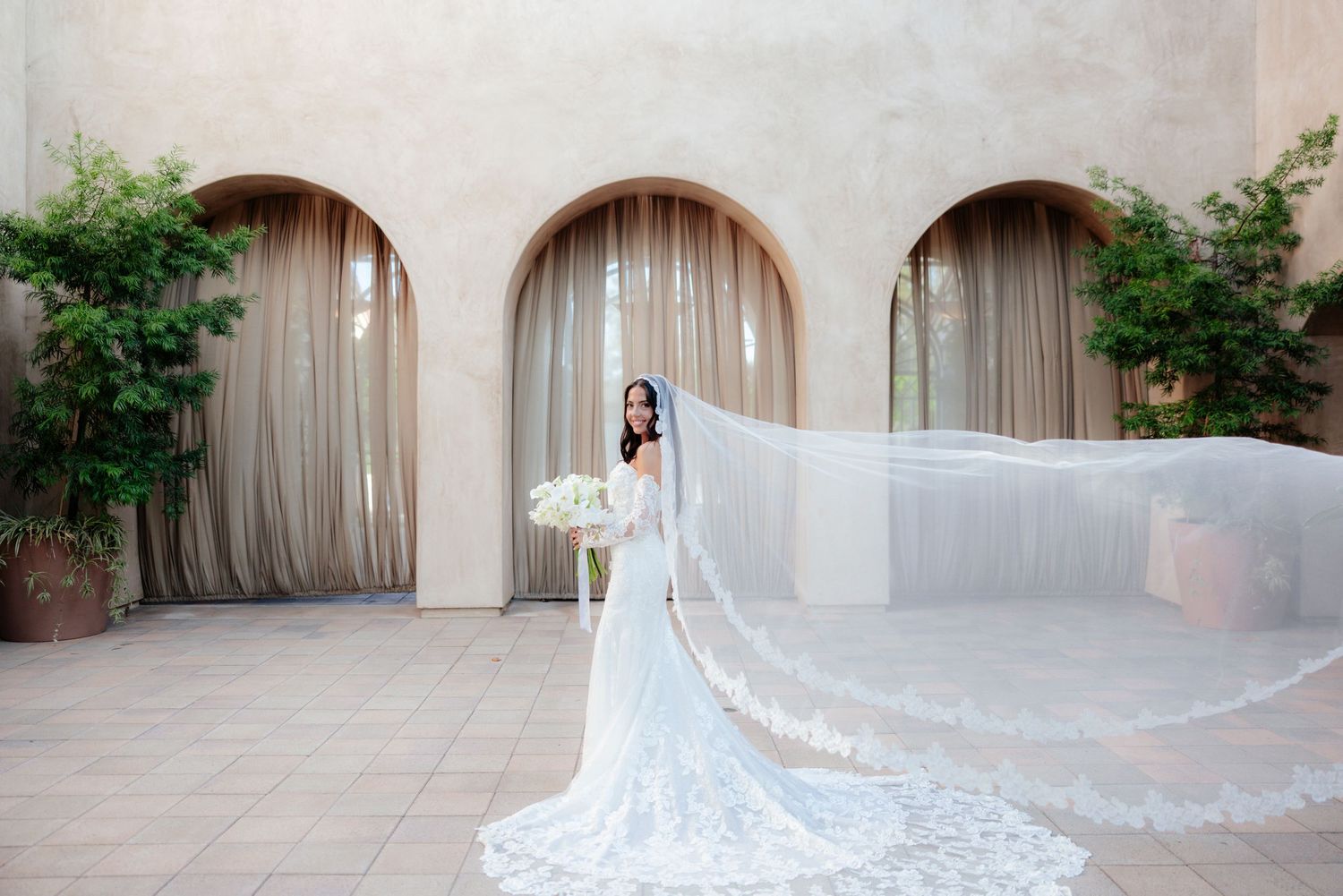 Wedding guests enjoy an elegant outdoor reception dinner under arches and palm trees at a luxury venue.