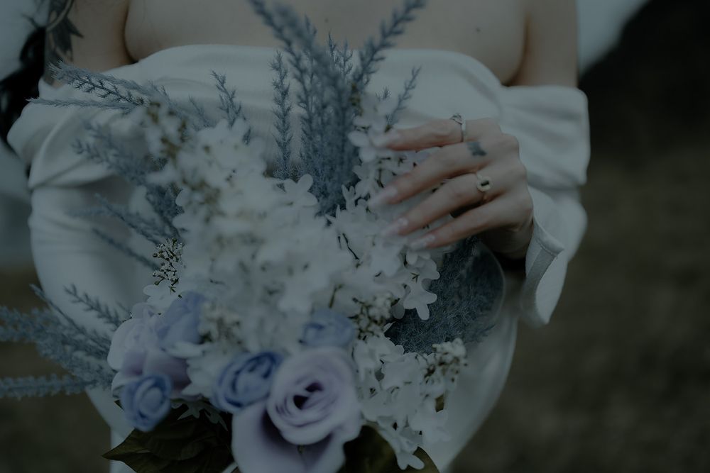 A bride holds a blue and white wedding bouquet with roses and wildflowers in a white dress.