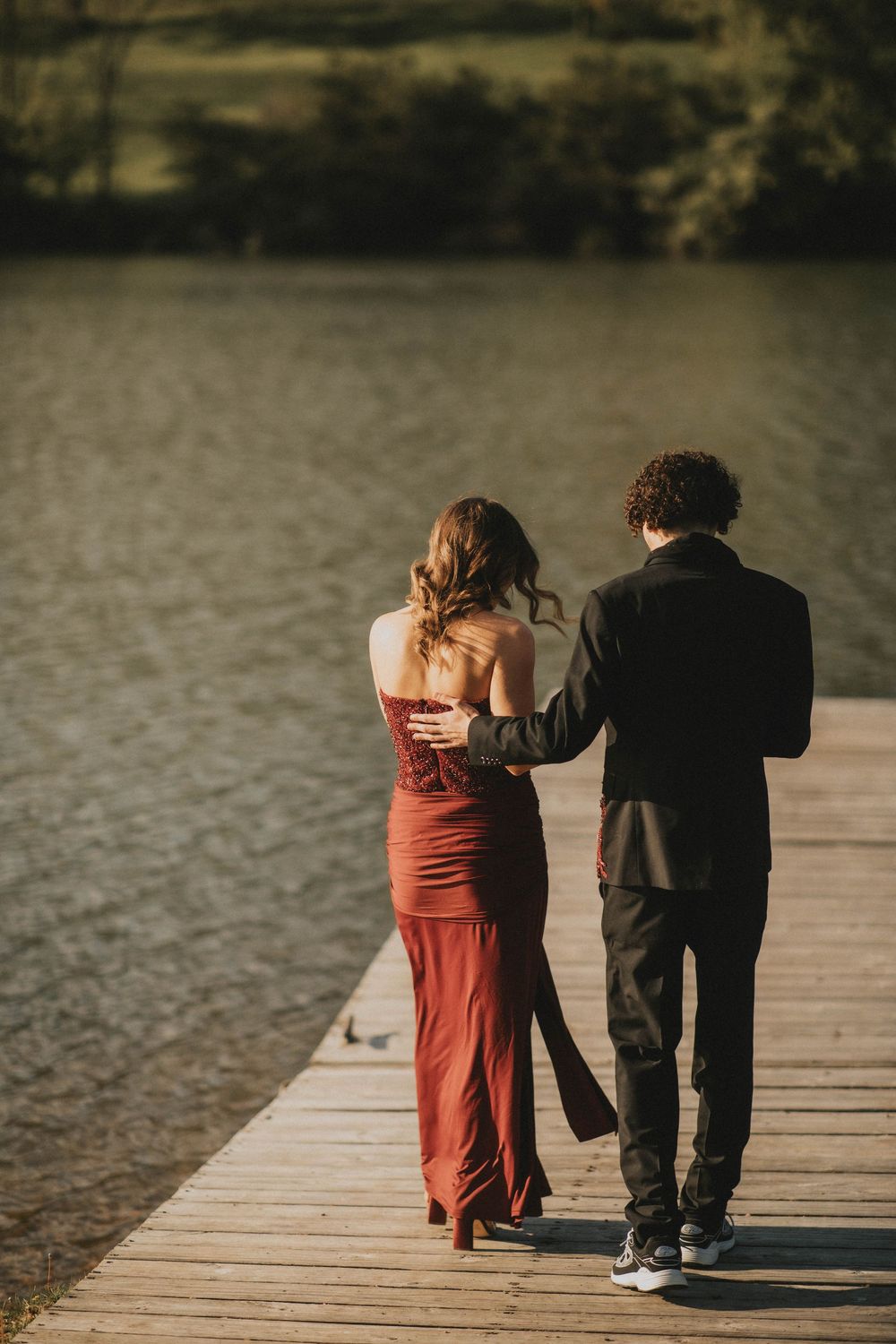 A couple in formal attire stands on a wooden dock by a lake, the woman in a red gown and man in black suit. indiana pa photographer prom