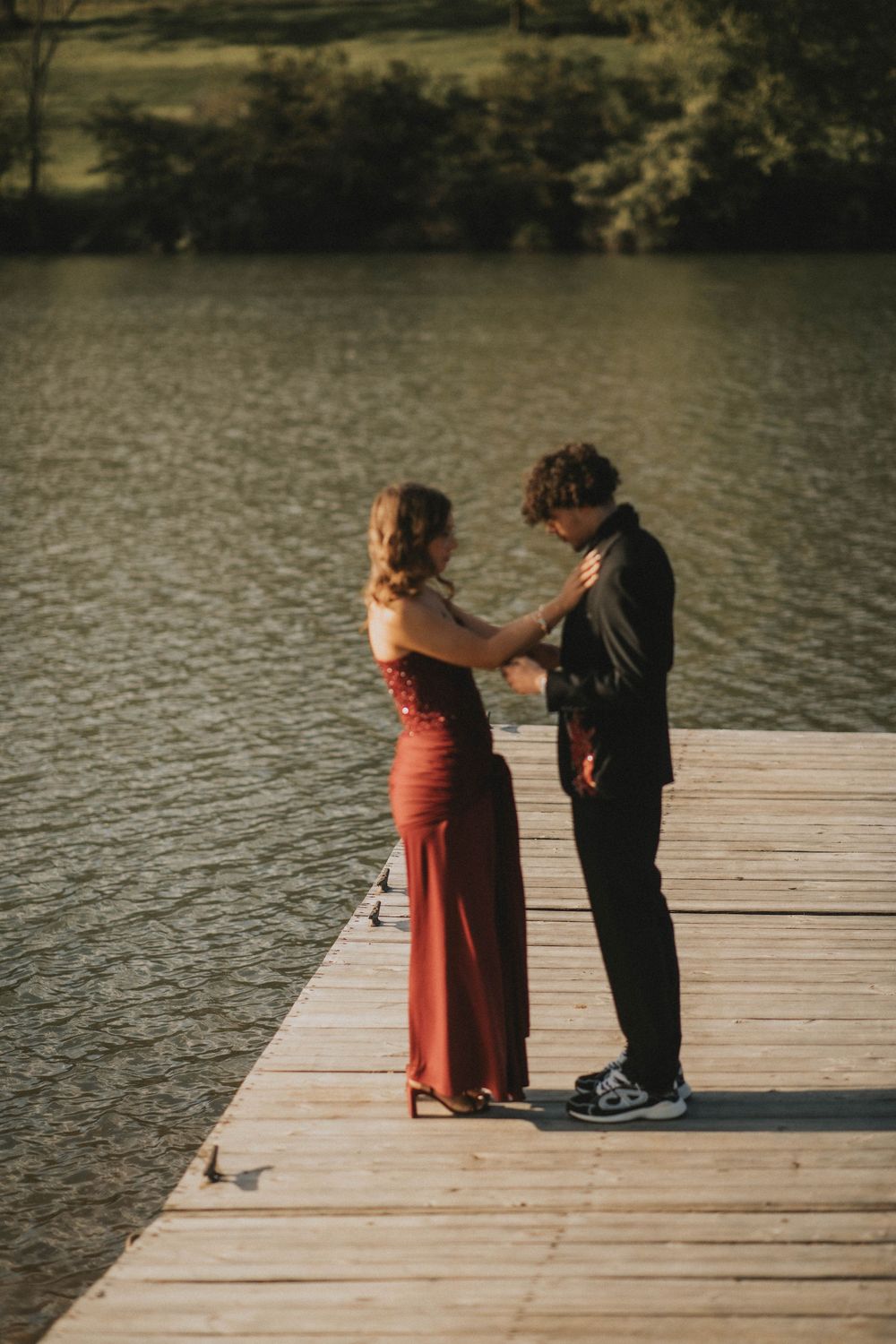 A couple in formal attire stands on a wooden dock by a lake, the woman in a red gown and man in black suit. indiana pa photographer prom
