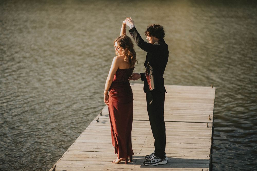A couple in formal attire stands on a wooden dock by a lake, the woman in a red gown and man in black suit. indiana pa photographer prom