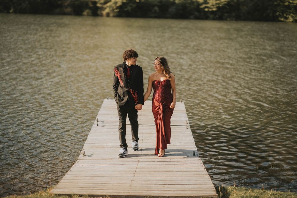 A couple in formal attire stands on a wooden dock by a lake, the woman in a red gown and man in black suit. indiana pa photographer prom
