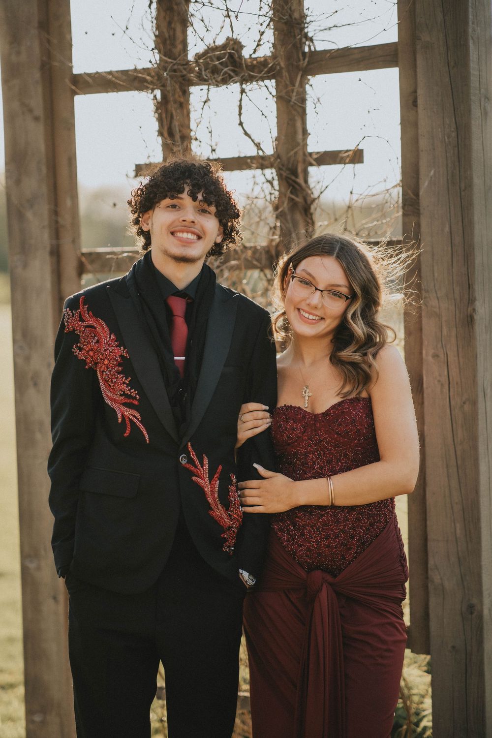 Couple embracing under a wooden pergola in a lush garden, wearing formal attire for a romantic outdoor photo. indiana pa photographer senior