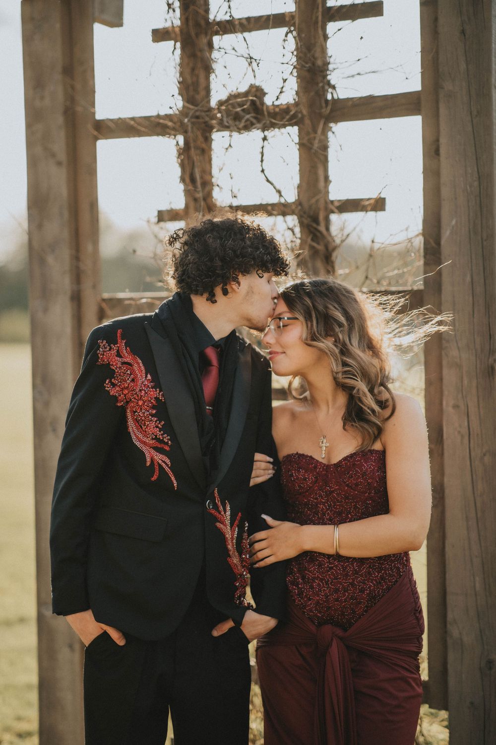 Couple embracing under a wooden pergola in a lush garden, wearing formal attire for a romantic outdoor photo. indiana pa photographer senior