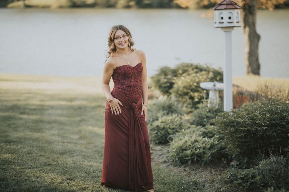 Young woman in elegant strapless burgundy gown posing outdoors near a birdhouse indiana pa photographer, senior in prom dress