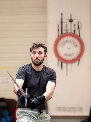 Un pratiquant d'escrime artistique, tout en concentration, s'entraînant aux techniques d'escrime à la "Formation aux armes"