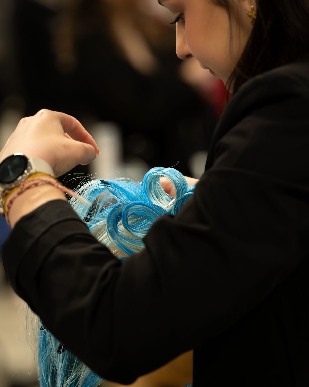 Une coiffeuse coiffe une perruque bleue bouclée sur une tête de mannequin lors d'un concours de coiffure. Meilleur Apprenti de France