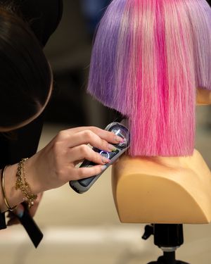Une apprentie réalise une coupe sur une tête de mannequin  aux couleurs vives, rose et violette lors du "Meilleur apprenti de France" Vendée