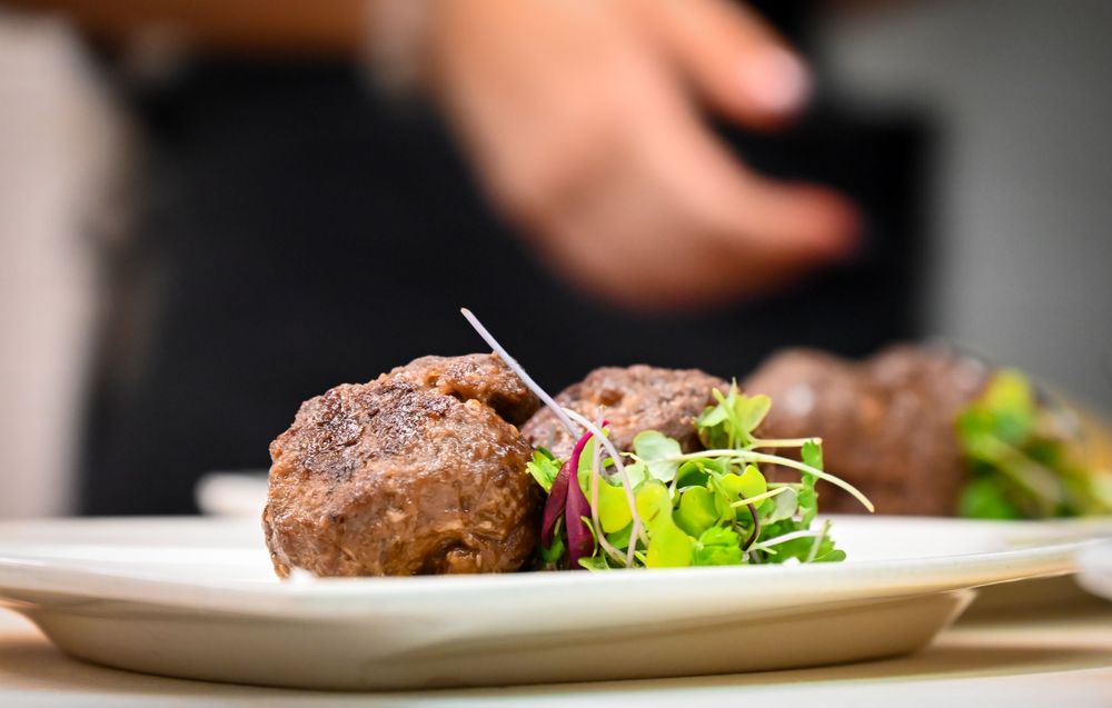 Gourmet meatballs garnished with fresh microgreens on a white plate, elegantly plated in a fine dining restaurant.