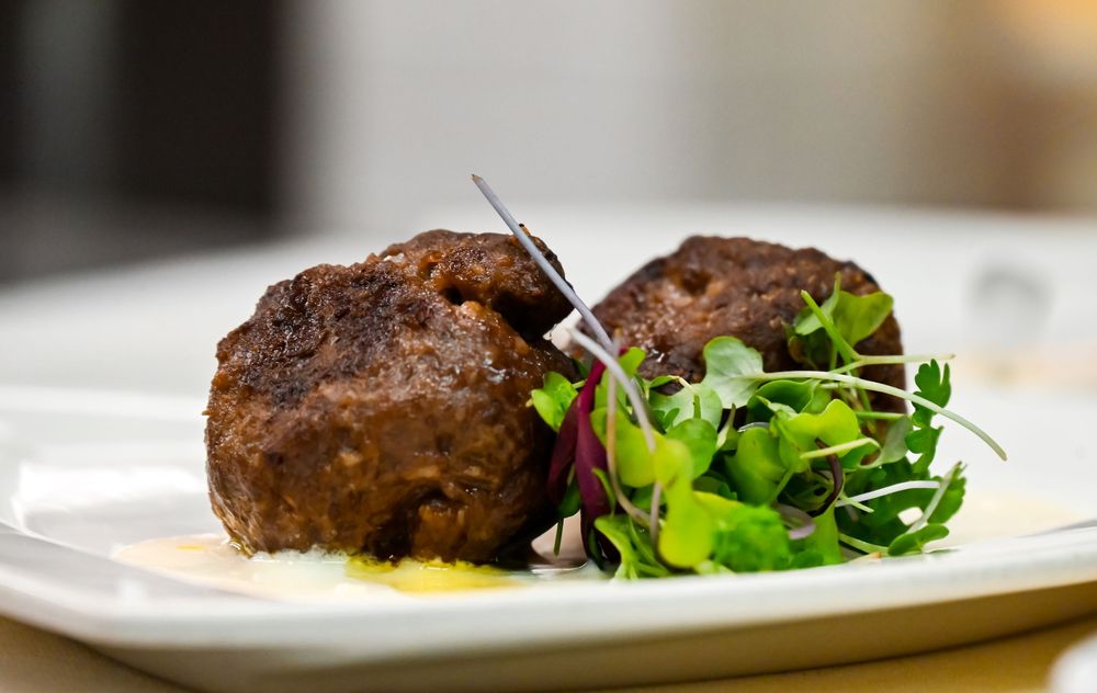 Two golden-brown meatballs served on a white plate with fresh microgreens and a drizzle of yellow sauce.