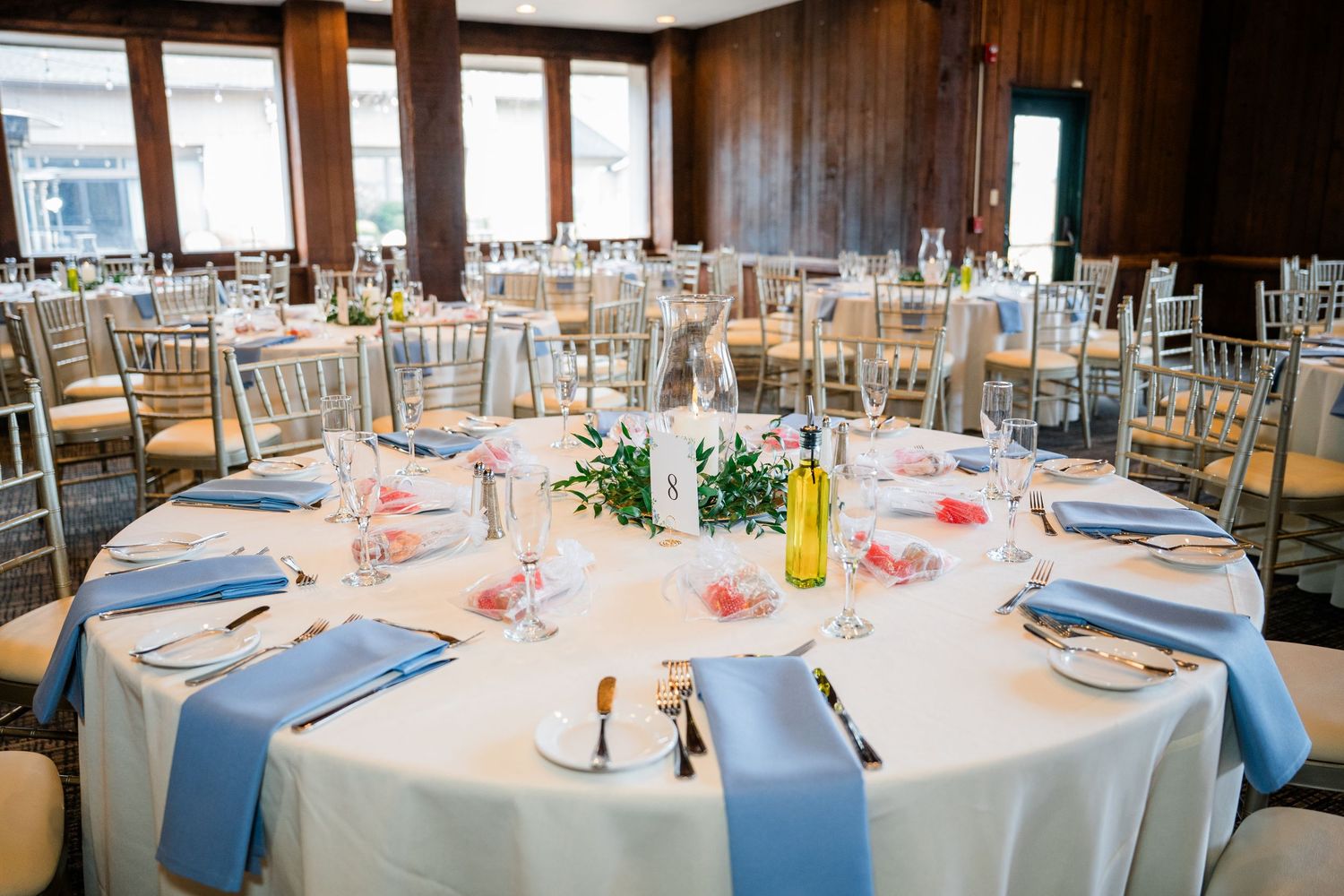 Elegant wedding reception hall with round tables, gold chairs, wood-paneled walls, and string lights overhead.