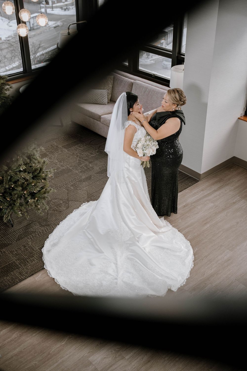 Overhead view of bride in white gown with long train being helped by woman in black dress.