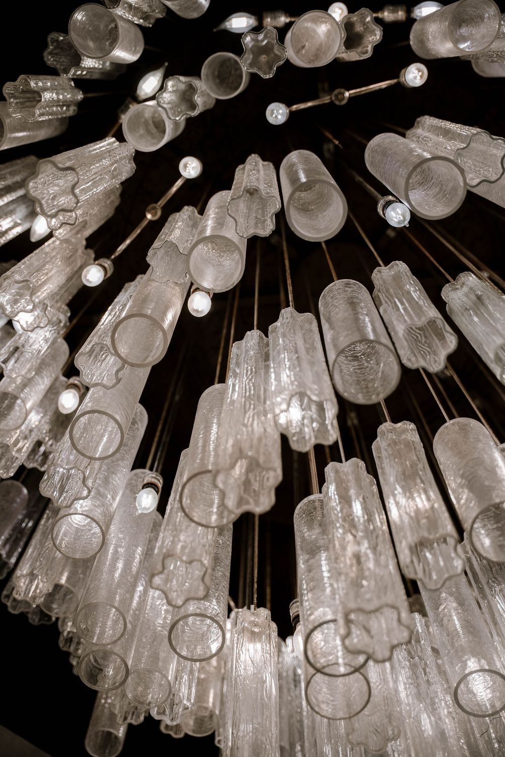 Stunning crystal glass chandelier with illuminated translucent pendants hanging against a dark ceiling.