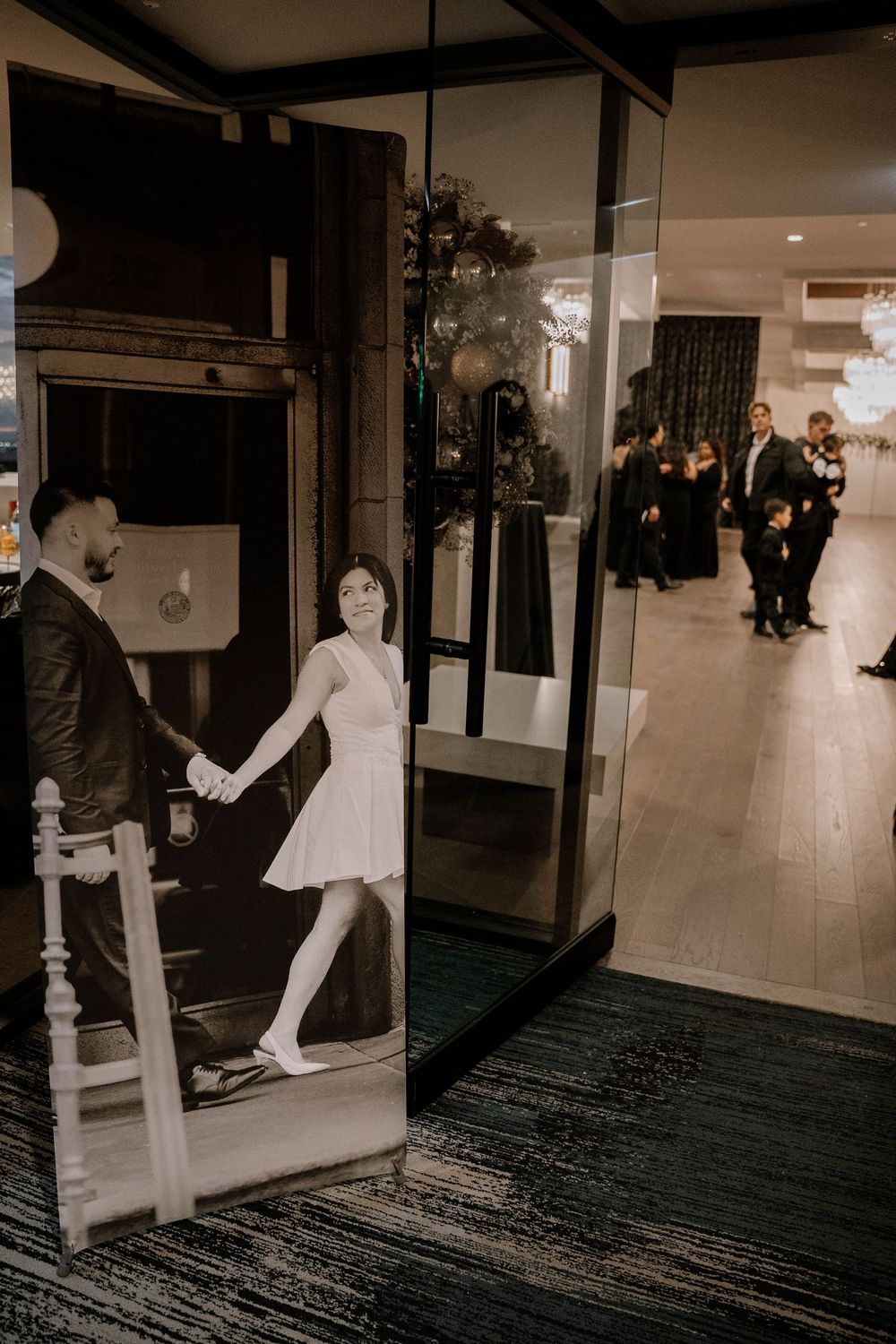 A black and white couple photo display at a wedding venue entrance with elegantly dressed guests in the background.
