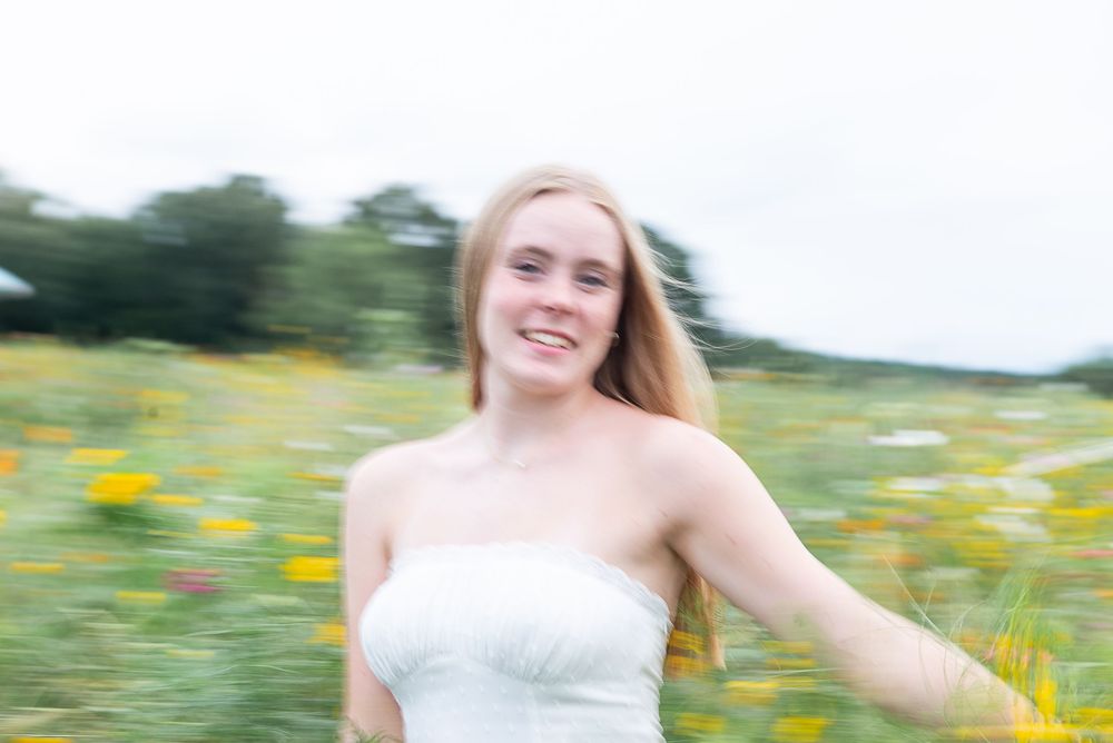 A person in a white dress walks through a sunny meadow filled with vibrant yellow wildflowers.