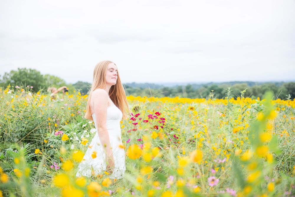 Person in white dress twirling joyfully among colorful summer wildflowers in a scenic meadow.