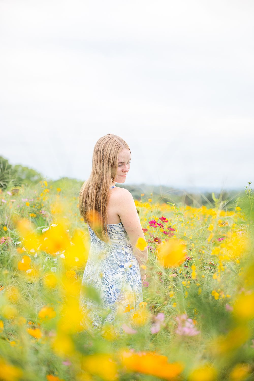 A dreamy portrait of someone in a floral dress standing in a vibrant field of yellow wildflowers on a summer day.