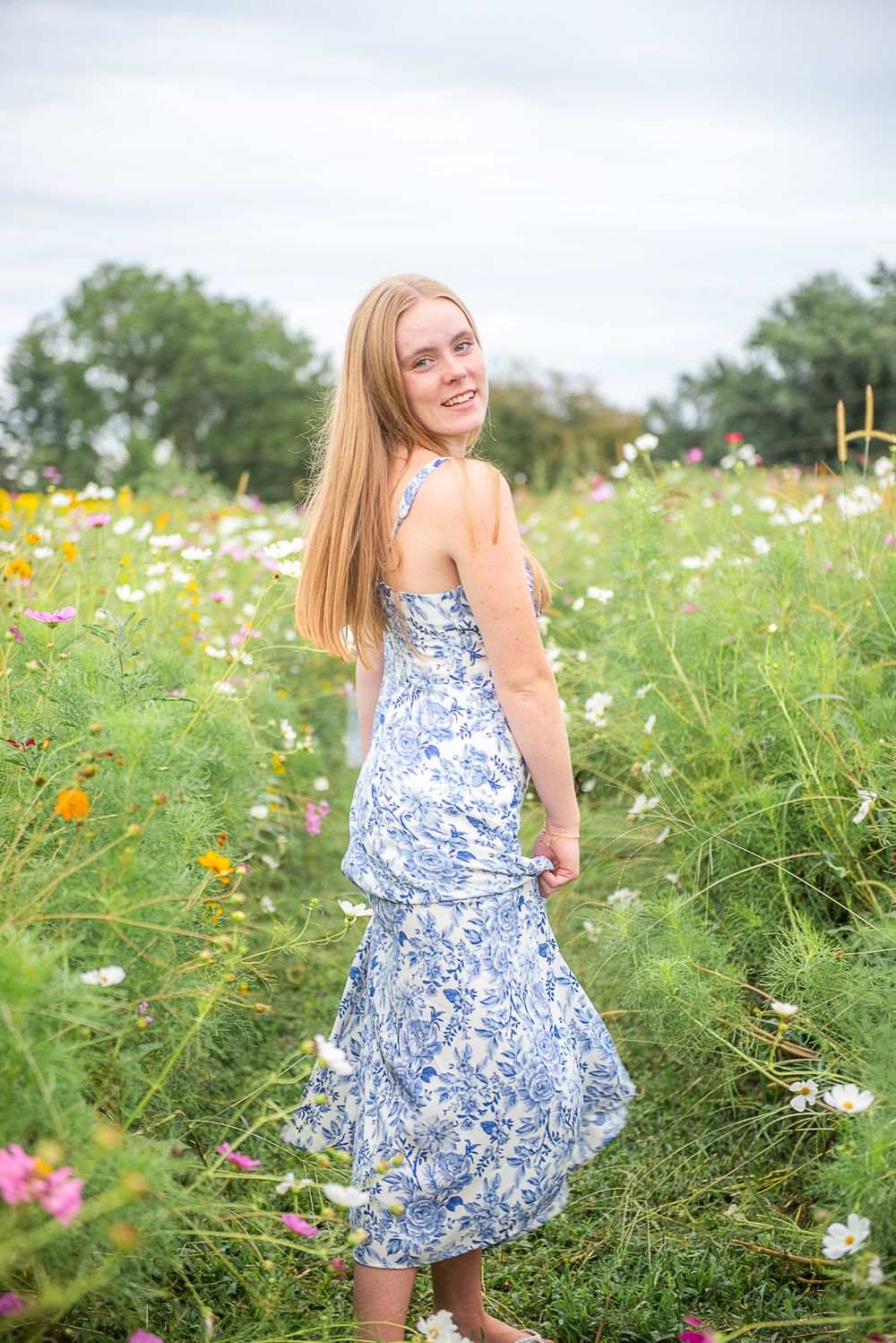 A blue and white floral dress flows gracefully in a summer wildflower field filled with colorful blooms.