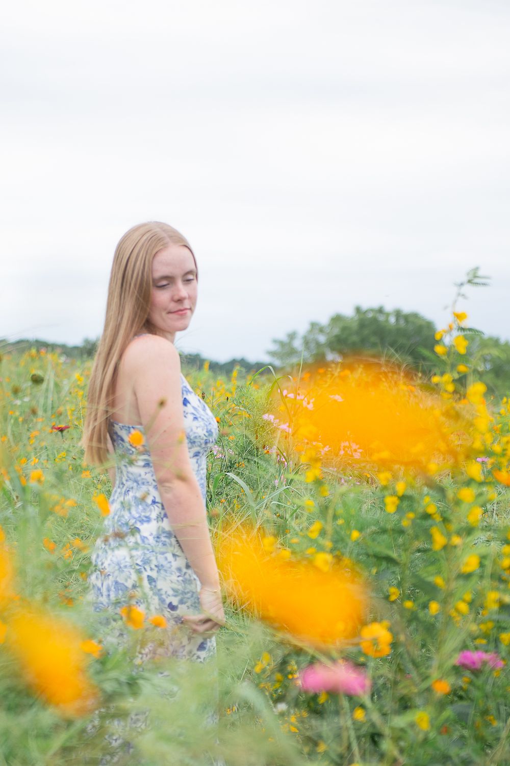 A candid outdoor portrait captured among blooming yellow and pink wildflowers in a sunny garden setting.