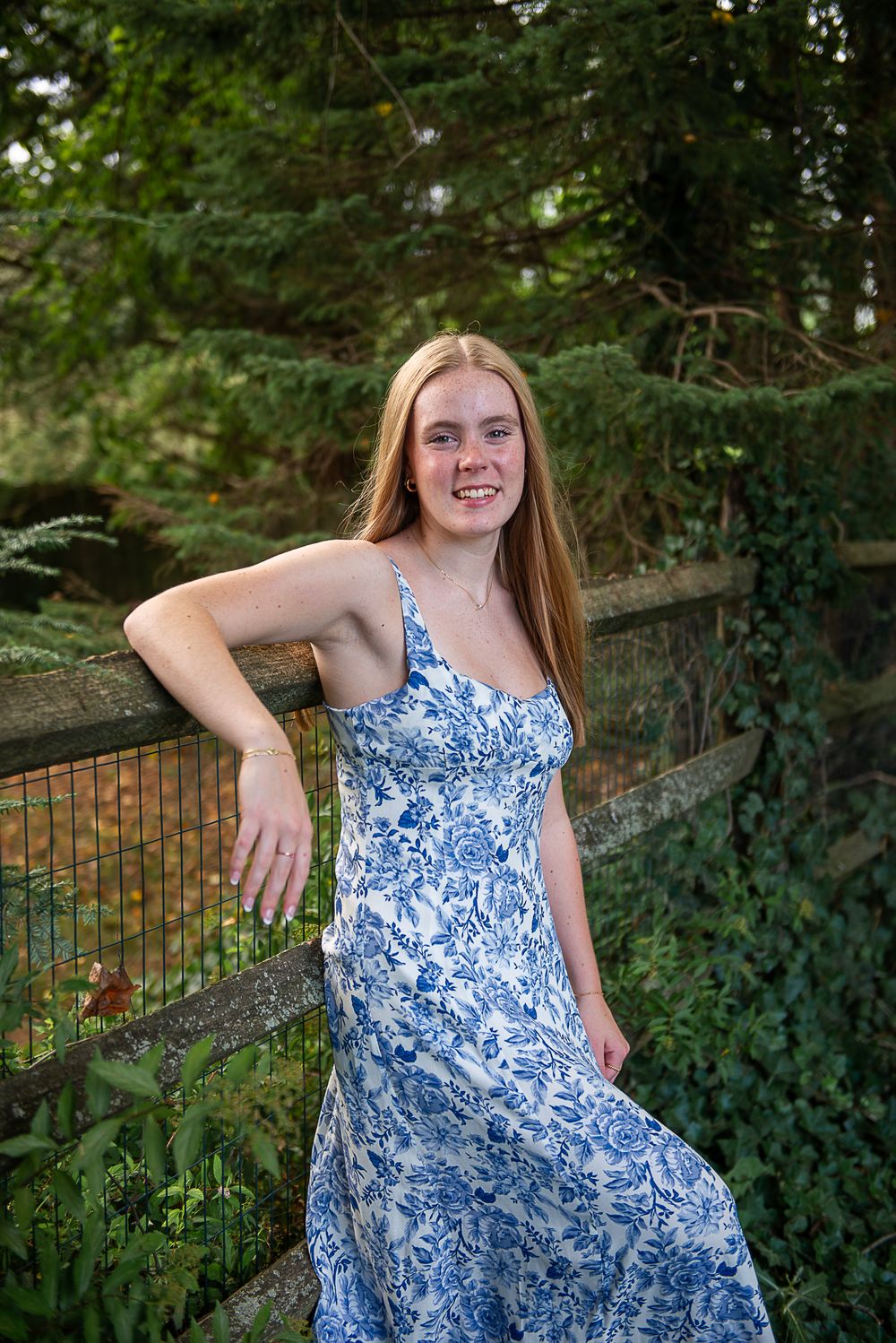 A blue and white patterned sundress is showcased against a backdrop of lush greenery and wooden fencing.